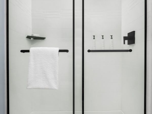 Modern walk-in shower with black fixtures, a towel bar, soap bottles, and a glass screen.