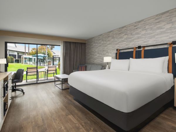 A modern hotel room with a king bed, side lamps, and large patio doors opening to a grassy courtyard.