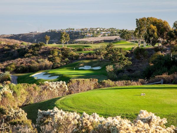 A sunny golf course with lush fairways and sand traps stretching toward distant homes on a hillside.