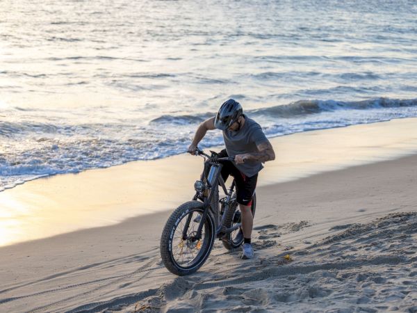 A cyclist rides a fat-tire bike along a sandy beach with waves rolling in behind him.