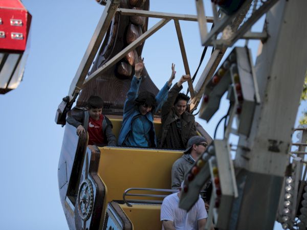 A group of people, including children, wave from an elevated open truck as workers stand nearby.