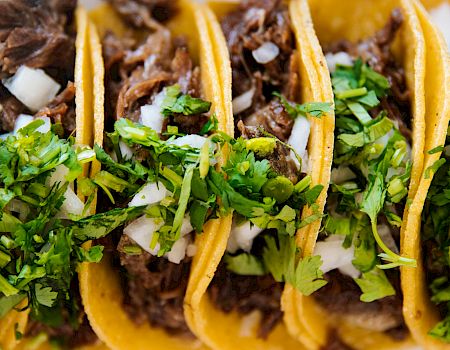 Close-up of tacos with crunchy yellow shells, savory meat, chopped onions, and fresh cilantro.