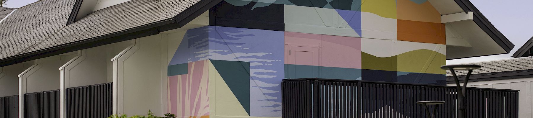 A house exterior with a colorful geometric mural on the side wall and a dark fence in front.
