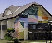 A house exterior with a colorful geometric mural on the side wall and a dark fence in front.