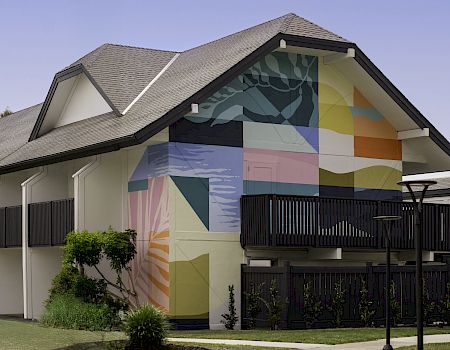 A house exterior with a colorful geometric mural on the side wall and a dark fence in front.