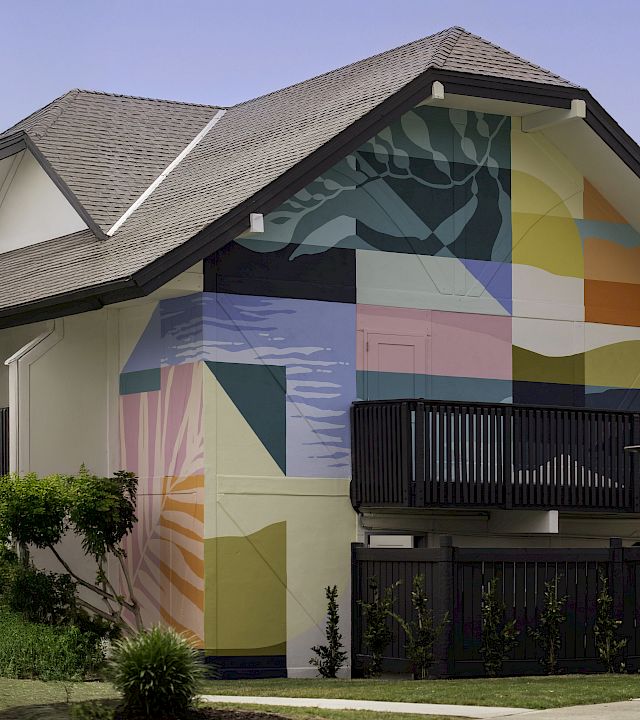 A house exterior with a colorful geometric mural on the side wall and a dark fence in front.