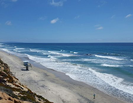 A scenic coastline beach with crashing waves, a lifeguard stand, sandy shore, and a bright blue sky.
