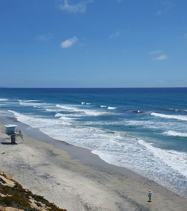A scenic coastline beach with crashing waves, a lifeguard stand, sandy shore, and a bright blue sky.