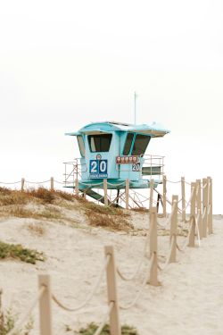 A blue lifeguard tower marked &ldquo;20&rdquo; stands on a sandy beach dune, with ropes and dunes in the foreground.