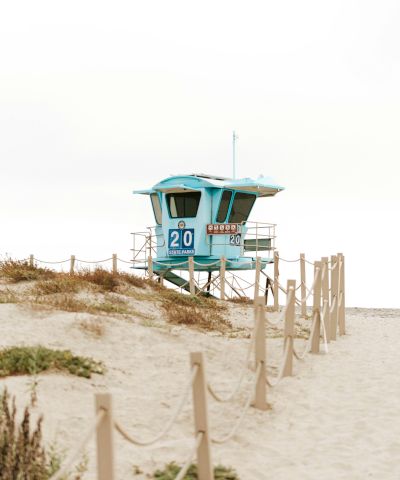 A blue lifeguard tower marked &ldquo;20&rdquo; stands on a sandy beach dune, with ropes and dunes in the foreground.