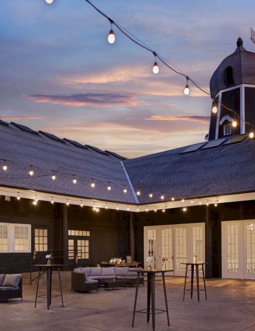 A cozy courtyard at dusk with string lights, warm lantern bulbs, and a windmill-style cupola on the roof.