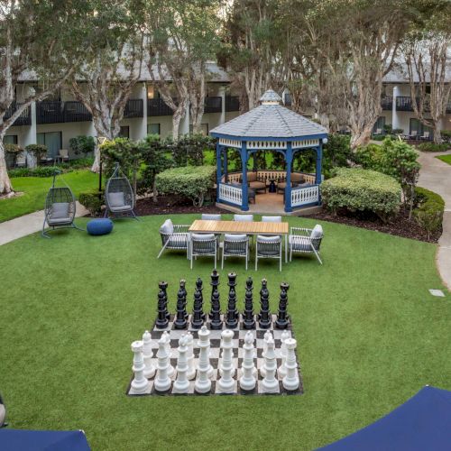 A landscaped resort courtyard with a blue gazebo, patio seating, and a large outdoor chess set on the lawn.