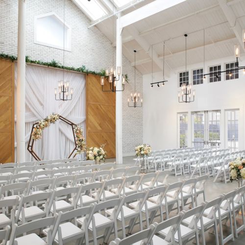 Bright wedding chapel with rows of white chairs, a floral arch, and hanging lantern lights.