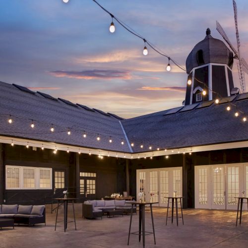 A cozy outdoor courtyard at dusk with string lights and a rustic windmill tower above the patio.