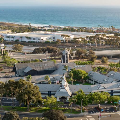 A coastal town view with ocean waves, houses and streets, plus a small white windmill near a sunny campus.