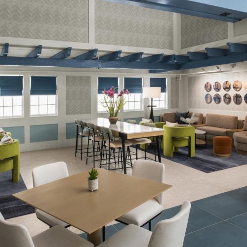 A modern lounge with blue blinds, a big sofa and coffee table, dining chairs, ceiling shelves, and framed circular wall art.