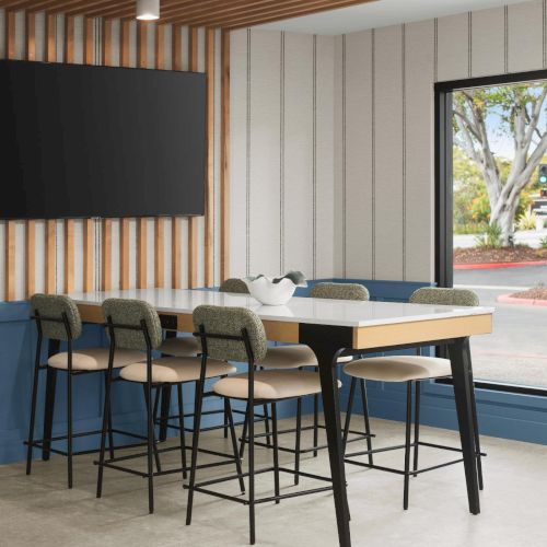 Modern covered patio with bar-height table, stools, wall-mounted TV, and a large open door showing trees outside.