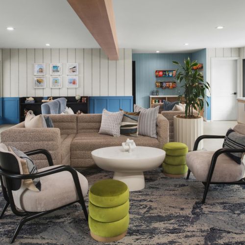 A modern lounge with a beige sectional sofa, accent chairs, coffee table, plants, and blue/striped walls.