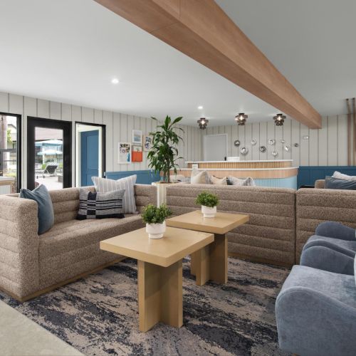 Bright modern living room with beige sectional couches, coffee tables, patterned rug, big windows, and hanging light fixtures.