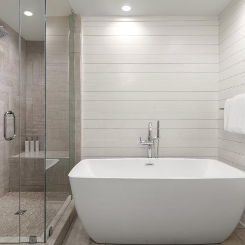 Modern bathroom with tiled shower, glass door, freestanding tub, wall-mounted showerhead, and folded white towels.