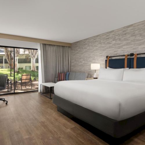A modern hotel bedroom with a large bed, bedside lamps, and floor-to-ceiling doors opening to a garden view.