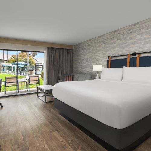 A modern hotel bedroom with a king bed, bedside lamps, and sliding doors opening to a garden.