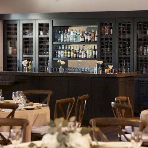 A restaurant bar with shelves of spirits, wine bottles, glassware, and tables set for a meal.
