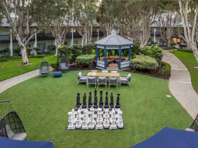 A hotel courtyard with a blue gazebo, patio furniture, and a giant chessboard set on the lawn.