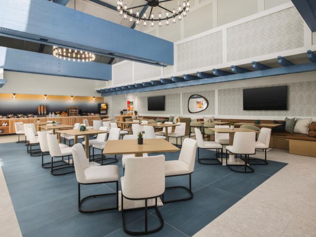 A modern hotel buffet lounge with a breakfast counter, many dining tables and chairs, and warm ceiling lights.