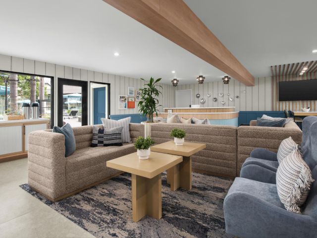 A modern lounge with beige sectional sofas, coffee tables, striped walls, pendant lights, and large windows.