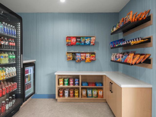 A snack and drink convenience corner: illuminated fridge and shelves stocked with chips, candy, and soda.