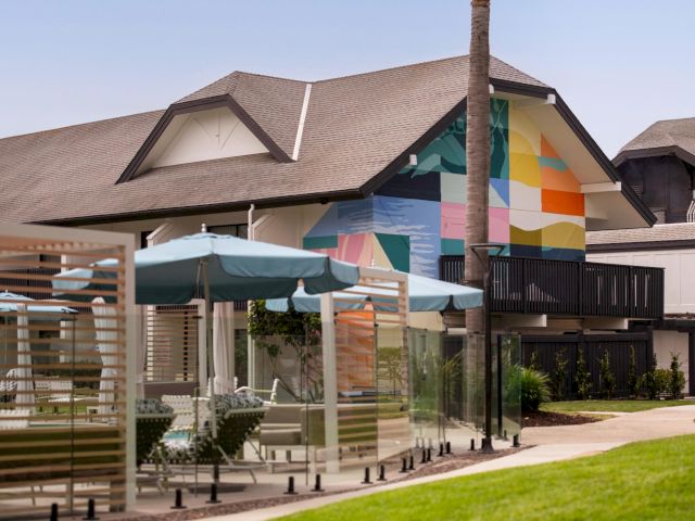 A modern home with a colorful mural on the wall, outdoor patio umbrellas, and a poolside walkway under a sunny sky.